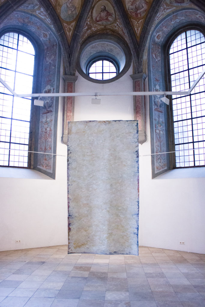 Das Bild zeigt die Ausstellungssituation der Arbeit "Die Grenzen der Ausdrucksfähigkeit" von Anna Weber in der St Anna Kapelle in Passau. Eine Monochrome Malerei hängt vor dem ehemaligen Altarraum der Kapelle.