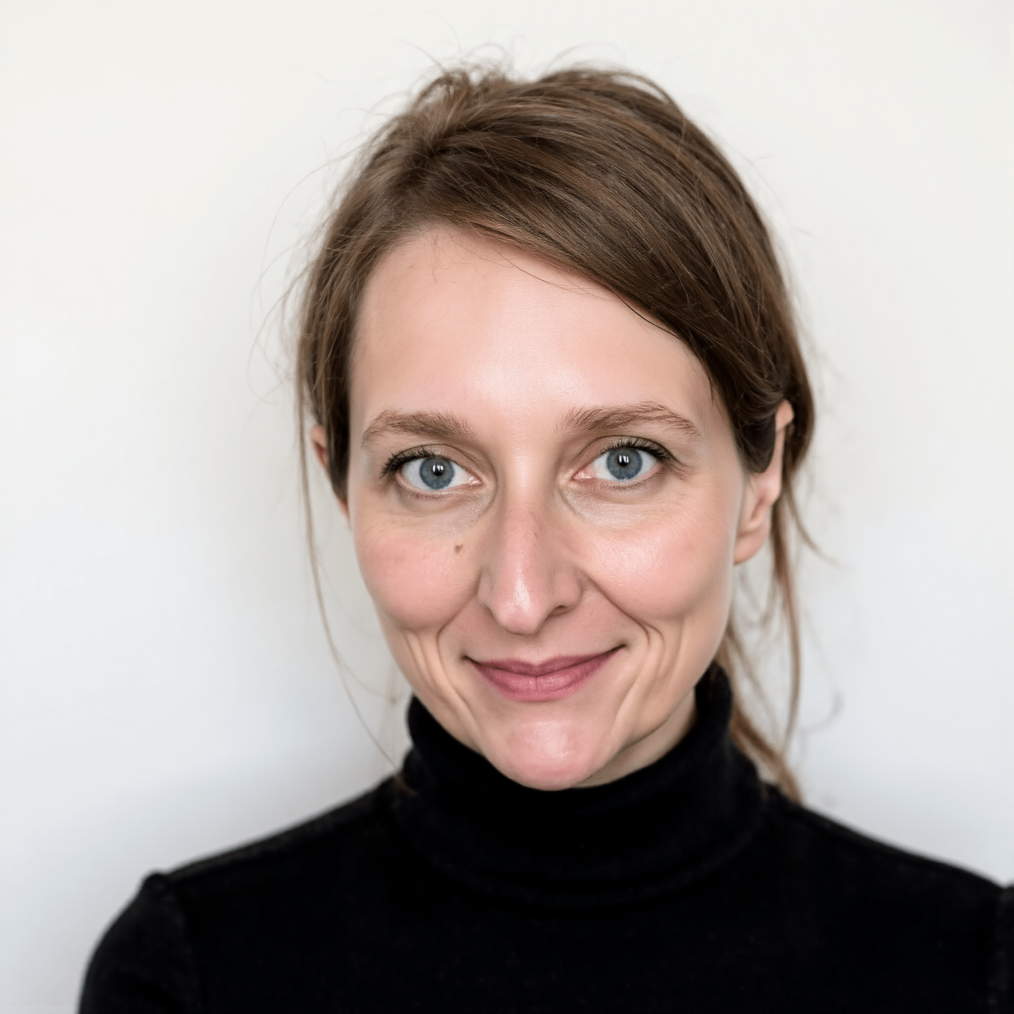 A portrait of a woman with light skin, blue eyes, and light brown hair tied back, wearing a black turtleneck, smiling gently with a neutral background